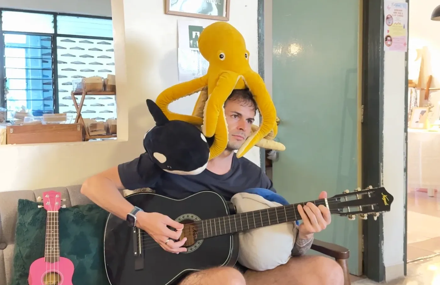 Tony joue de la guitare, une pieuvre en peluche sur la tête et une orque sur l'épaule.